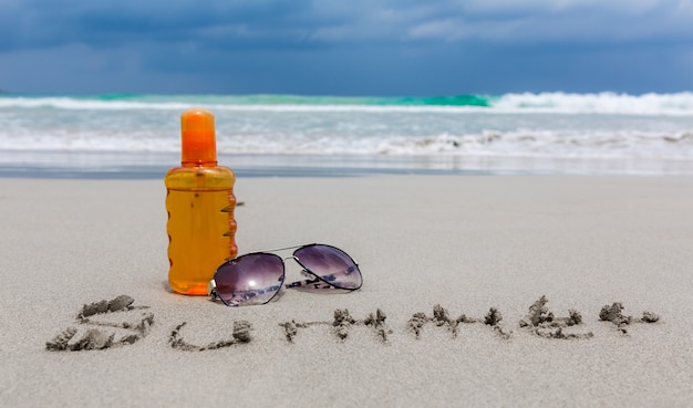 loción de protección solar y gafas oscuras en la playa para el verano