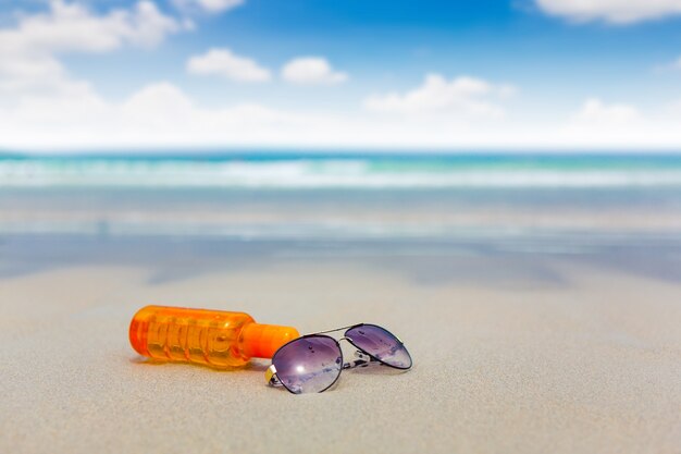 loción de protección solar y gafas oscuras en la playa para el verano