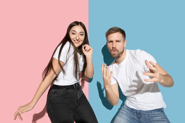 Loco. Bailar, moverse, divertirse. Hombre y mujer joven y feliz en ropa casual en pared bicolor rosa, azul. Concepto de emociones humanas, expresión facial, relaciones, anuncio. Hermosa pareja.