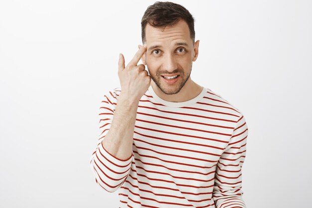 Estas loco. Retrato de novio guapo cabreado en jersey de rayas, dedo índice rodante