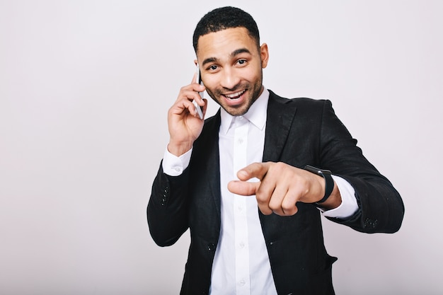 Lograr un gran éxito en la carrera del joven apuesto con camisa blanca, chaqueta negra hablando por teléfono. Hombre de negocios elegante, sonriendo, expresando felicidad, buena suerte.