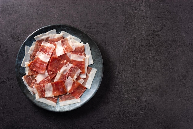 Lonchas de jamón serrano español sobre placa negra sobre fondo de pizarra negra