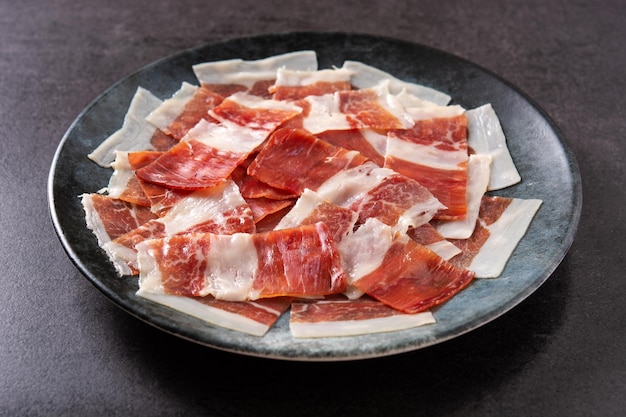 Lonchas de jamón serrano español sobre placa negra sobre fondo de pizarra negra