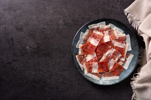 Lonchas de jamón serrano español sobre placa negra sobre fondo de pizarra negra