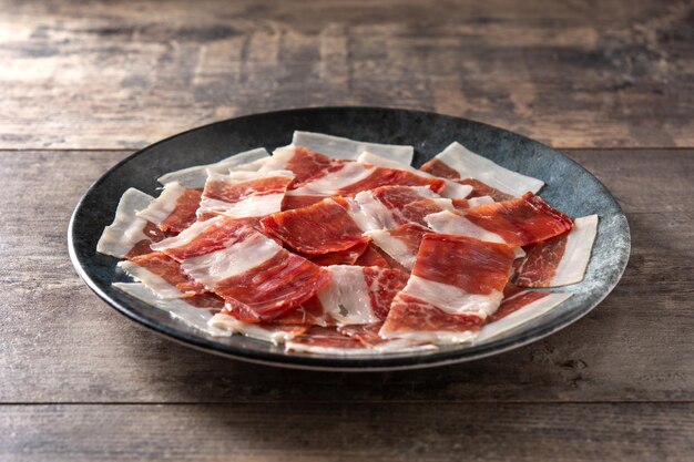 Lonchas de jamón serrano español sobre placa negra sobre mesa de madera