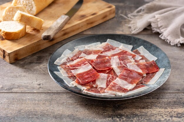 Lonchas de jamón serrano español sobre placa negra sobre mesa de madera