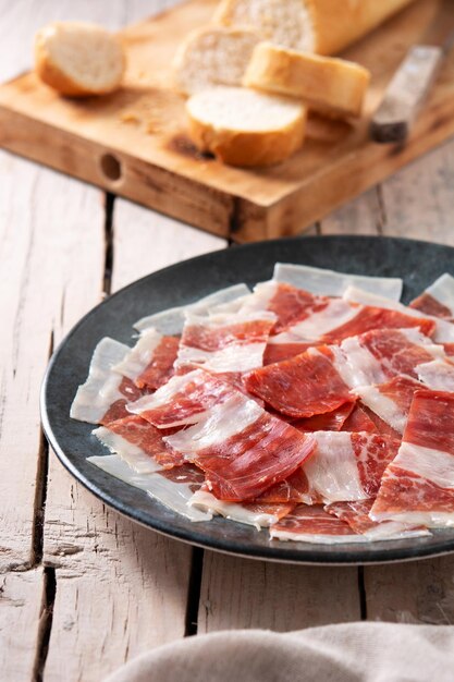 Lonchas de jamón serrano español sobre placa negra sobre mesa de madera