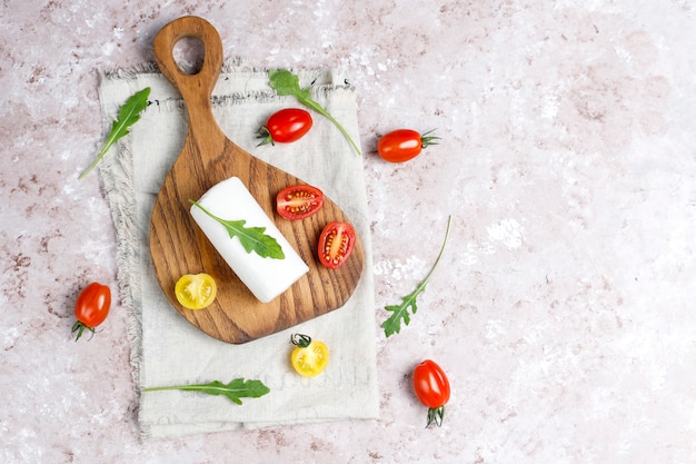 Lonchas de queso de cabra sobre tabla de madera con ruccola, tomates cherry. Listo para comer.