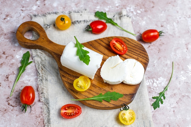 Lonchas de queso de cabra sobre tabla de madera con ruccola, tomates cherry. Listo para comer.