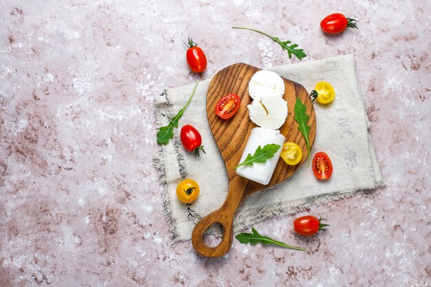 Lonchas de queso de cabra sobre tabla de madera con ruccola, tomates cherry. Listo para comer.