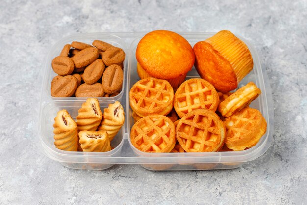 Lonchera poco saludable con galletas, waffles, muffins en superficie de concreto