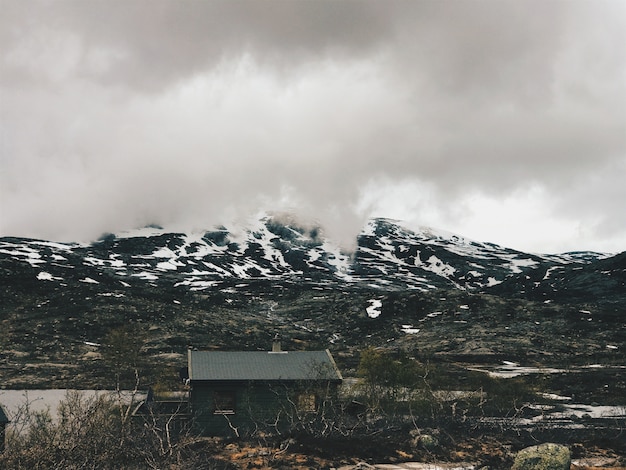 Foto gratuita lonely cabina se encuentra ante las montañas cubiertas de nieve