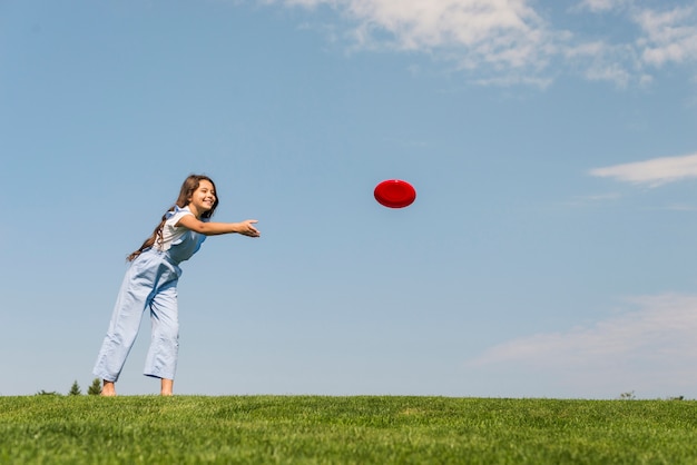 Foto gratuita long shot niña jugando con frisbee rojo