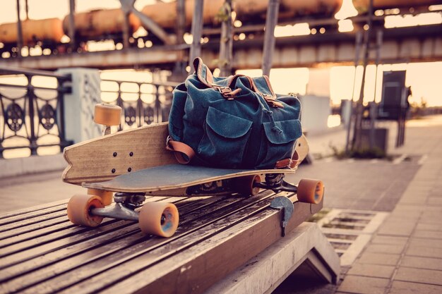 Longboard y mochila en un banco de una ciudad.