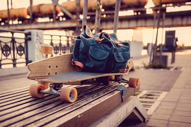 Longboard y mochila en un banco de una ciudad.