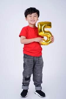 Longitud total del cuerpo de la sonrisa feliz del niño pequeño asiático con el globo del número de la hoja, aislado