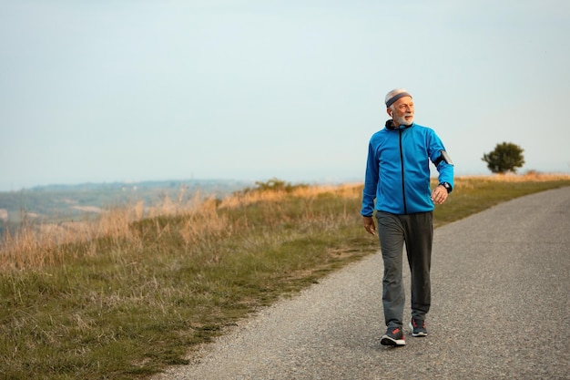 Longitud total de deportista senior dando un paseo por la mañana y escuchando música con auriculares en la naturaleza Copiar espacio