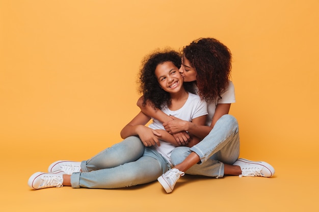 Longitud total de dos hermanas africanas felices sentados y besándose