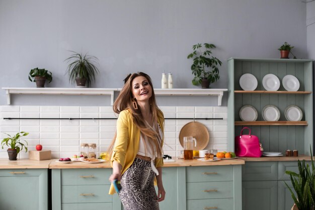 Longitud total de hermosa morena con ropa de moda y tacones bailando en la cocina Sintiéndose feliz por la mañana Interior moderno