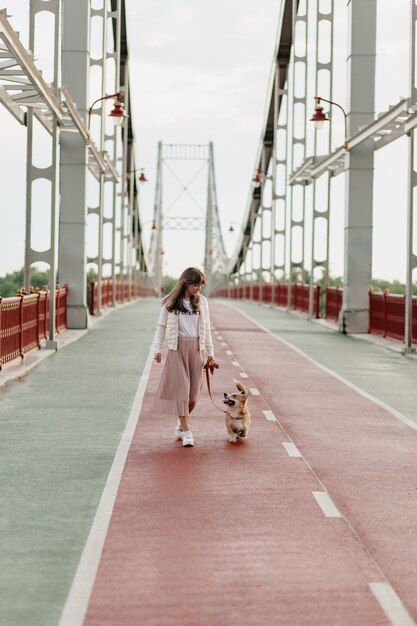 Longitud total de mujer caminando en puente brillante caminando con corgi