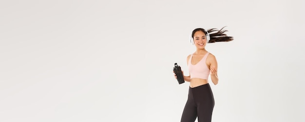 Longitud total de sonriente atractiva atleta femenina asiática haciendo ejercicio físico en el gimnasio deportista