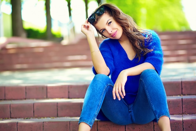 Foto gratuita look de alta moda glamour elegante sexy sonriente hermosa sensual joven modelo en tela brillante hipster de verano en blue jeans sentado en la calle