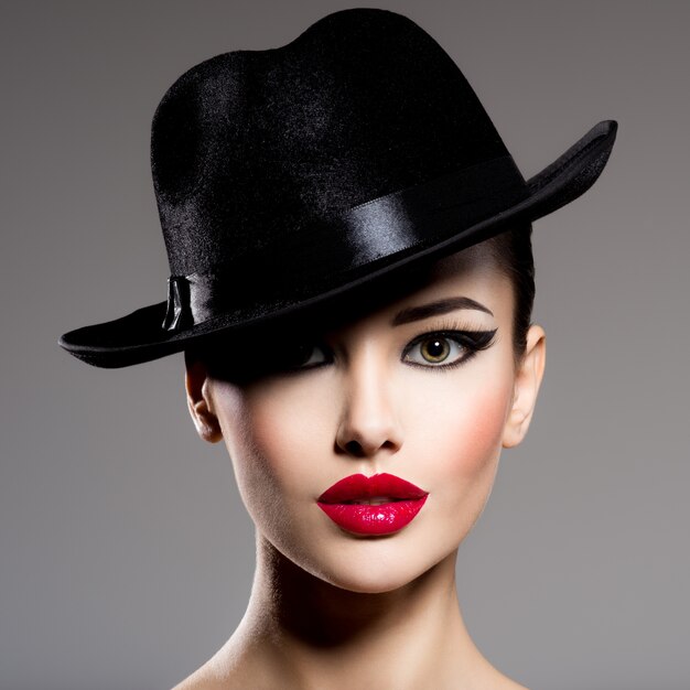 Сlose-up retrato de una mujer con un sombrero negro con labios rojos posando