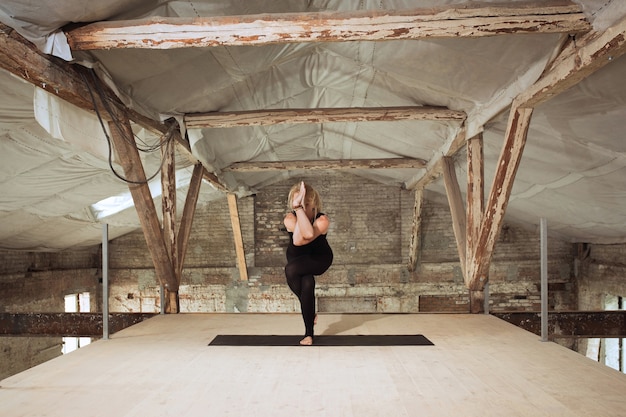 Loto. Una joven atlética ejercita yoga en un edificio de construcción abandonado. Equilibrio de salud mental y física. Concepto de estilo de vida saludable, deporte, actividad, pérdida de peso, concentración.