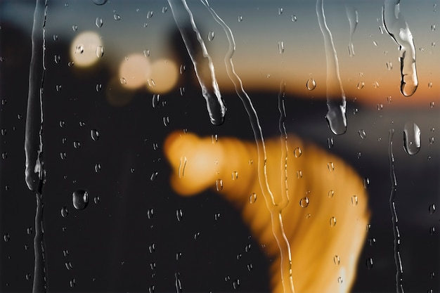 Luces de bokeh en la noche a través de la ventana con gotas de lluvia