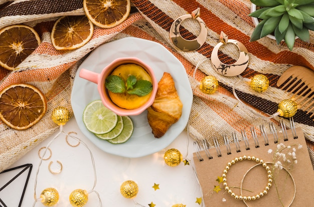 Luces decorativas doradas con accesorios femeninos y taza de té sobre fondo blanco