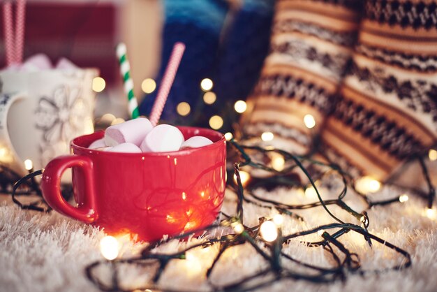 Luces de Navidad y taza de chocolate con malvavisco sobre alfombra