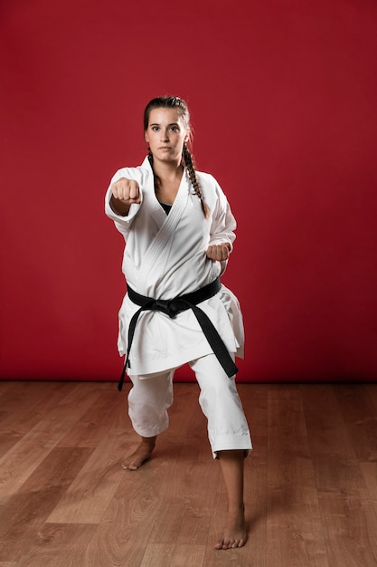 Foto gratuita luchador de karate femenino realizando golpe aislado sobre fondo rojo.