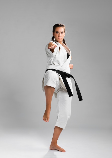 Luchador de karate femenino realizando patada aislado sobre fondo gris
