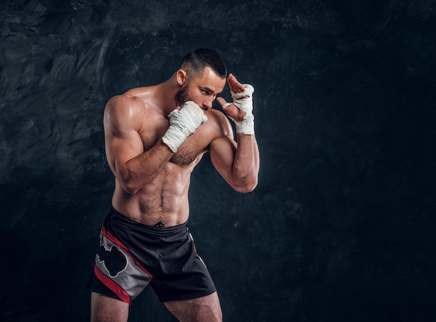 Un luchador musculoso fuerte muestra su golpe mientras posa para el fotógrafo en un estudio fotográfico oscuro.