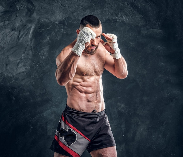 Foto gratuita un luchador musculoso fuerte muestra su golpe mientras posa para el fotógrafo en un estudio fotográfico oscuro.