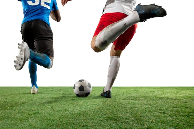 Luchando. Cerrar las piernas del fútbol profesional, jugadores de fútbol que luchan por la pelota en el campo aislado en la pared blanca. Concepto de acción, movimiento, emoción de alta tensión durante el juego. Imagen recortada.