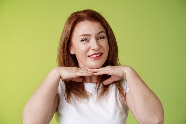 Luciendo bien, feliz, alegre, pelirroja, mujer de mediana edad, sonriente, encantado, tomarse de las manos debajo de la barbilla, aceptar defectos con imperfecciones, como la propia condición de la piel