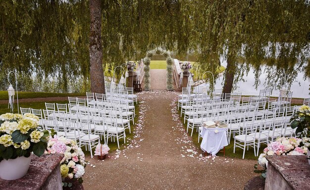Lugar para la ceremonia de boda con arco de boda decorado con flores y sillas blancas a cada lado del arco al aire libre. Preparación para la ceremonia de boda al aire libre cerca del lago.