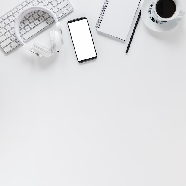 Lugar de trabajo con dispositivos electrónicos, papelería y taza de café en mesa blanca