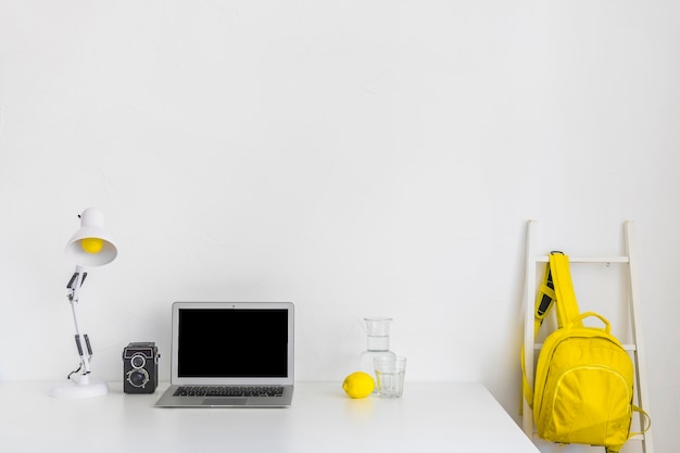 Lugar de trabajo elegante en colores blanco y amarillo con mochila y portátil