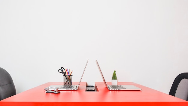 Lugar de trabajo moderno con dos computadoras portátiles en la mesa roja contra la pared blanca