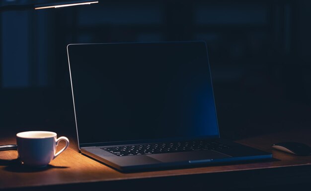 Lugar de trabajo en la oficina con computadora portátil y café en la habitación oscura por la noche