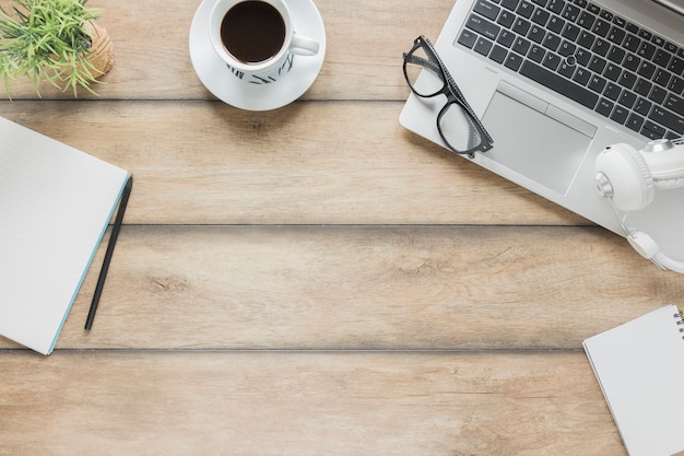 Lugar de trabajo con papelería, dispositivos electrónicos y taza de café en la mesa de madera.