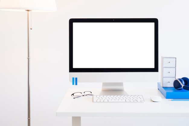 Lugar de trabajo con teclado cerca del monitor, lentes y audífonos cerca de la lámpara