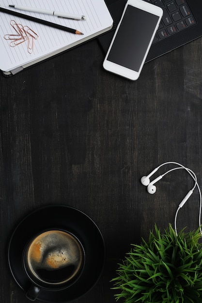 Foto gratuita lugar de trabajo con teléfono inteligente, taza de café, cuaderno, en mesa negra. vista superior de fondo