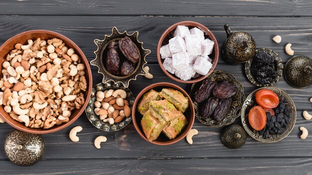 Lukum; fechas; frutas secas; Baklava y nueces en tazón de tierra y metálico en el escritorio de madera