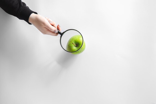 Lupa con manzana verde sobre fondo blanco.