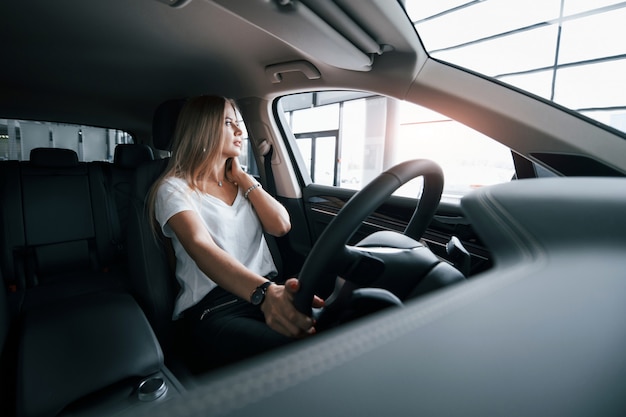 Luz natural. Chica en coche moderno en el salón. Durante el día en interiores. Comprar vehículo nuevo