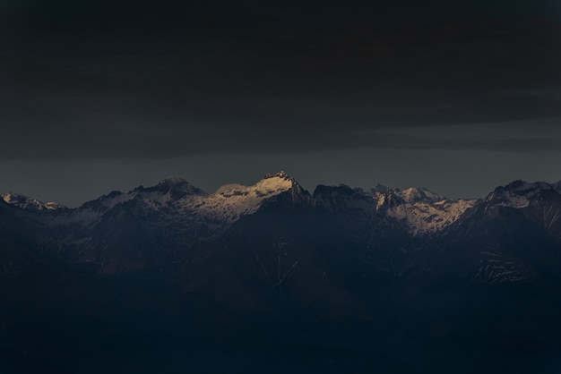 La luz del sol brillando en la cima de una montaña al atardecer con cielo nublado oscuro