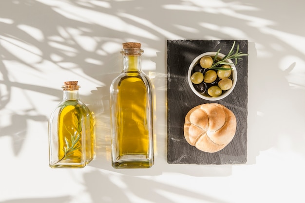 La luz del sol sobre las botellas de aceite de oliva con bollo y aceitunas en la placa de pizarra